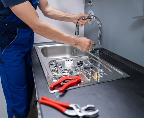 Professional plumber repairing and installing a kitchen sink tap with plumbing tools on the countertop in Tipton and Wolverhampton